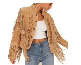 Puede incluir: Chaqueta de ante color canela con flecos largos en las mangas y la espalda. La chaqueta tiene una botonadura frontal y costuras decorativas. El cuello es de estilo alzado. La chaqueta es de color neutro y es adecuada para varios conjuntos.