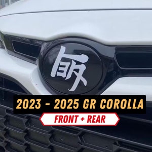 May include: A white 2023-2025 GR Corolla with a black front grille and a black emblem with white Japanese characters that say "GR". The text "FRONT + REAR" is written in red on a white background.
