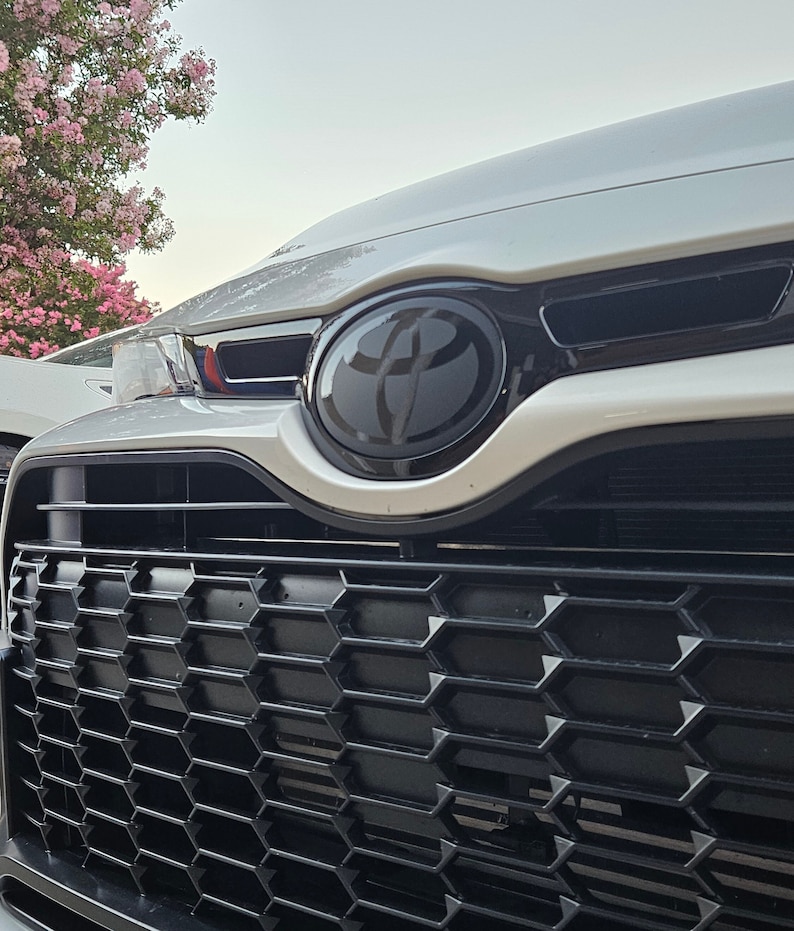 May include: Close-up of a white car's front grille with a black honeycomb pattern and a black Toyota emblem.