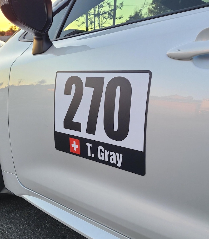 May include: A rectangular car door decal featuring the number 270 in large black font on a white background, with a black horizontal bar below containing a small Swiss flag icon and the white text T. Gray applied to a silver vehicle door.