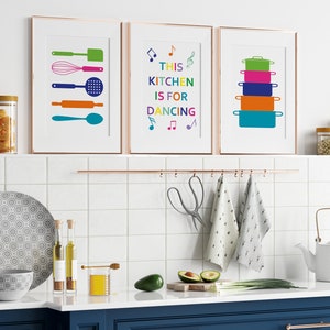 May include: Three framed prints with colourful kitchen-themed designs. The left print features a set of kitchen utensils, the middle print says "This Kitchen is for Dancing" with musical notes, and the right print shows a stack of colourful pots.