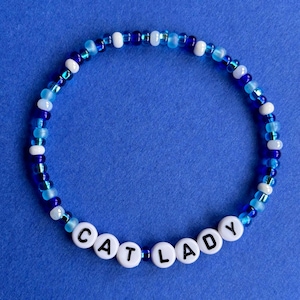 May include: A blue and white beaded bracelet with the word "CAT LADY" spelled out in white beads.