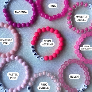 Puede incluir: Surtido de pulseras de cuentas de colores con diferentes colores y textos, incluyendo "Happy", "Magenta", "Neon Hot Pink", "Lemonade Pink", "Pastel Pink", "Pink Bubble", "Magenta Bubble", "Neon Bubblegum" y "Blush".