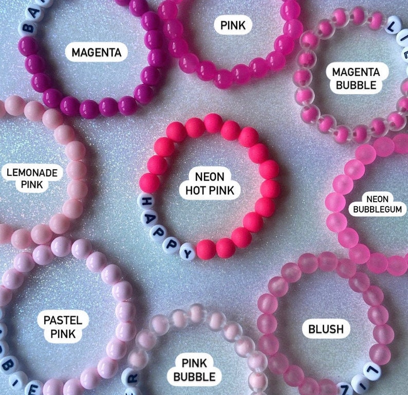 Puede incluir: Surtido de pulseras de cuentas de colores con diferentes colores y textos, incluyendo "Happy", "Magenta", "Neon Hot Pink", "Lemonade Pink", "Pastel Pink", "Pink Bubble", "Magenta Bubble", "Neon Bubblegum" y "Blush".
