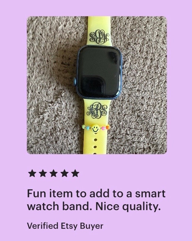 May include: A yellow silicone watch band with a black monogram on each side. The band is on a smartwatch with a black face.