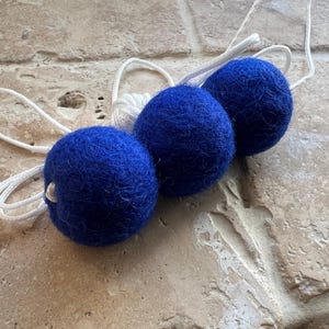 May include: Three blue felt balls strung together with white string. The balls are soft and fluffy.