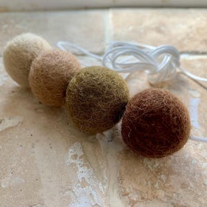 May include: A garland of felt balls in shades of brown, beige, and green. The balls are strung together with white twine.