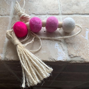 May include: A pink and white felt ball garland with a natural jute tassel. The garland is strung on a natural twine.