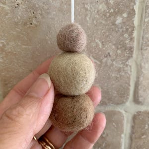 May include: A set of three felt balls in shades of brown, beige, and light brown. The balls are strung together and hang from a white string.