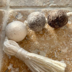 May include: A white, grey, and brown felt ball garland with a white tassel. The garland is made of wool felt balls and is perfect for adding a touch of rustic charm to your home decor.