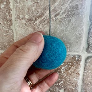May include: A teal blue felt ball with a thin silver string attached to it.