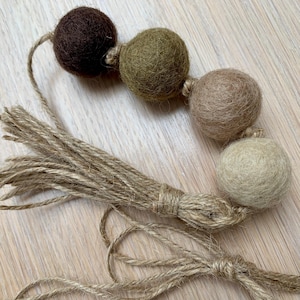 May include: A garland of brown, green and beige felt balls strung together with twine. The garland has a long tassel of twine.