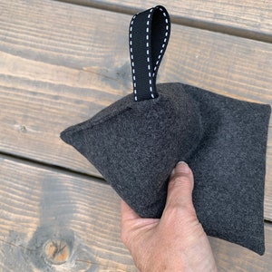 May include: A gray felt doorstop with a black fabric handle. The handle has white stitching.