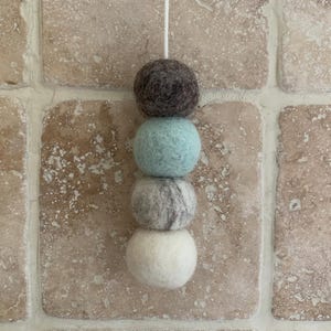 May include: A string of four felt balls hanging from a white string. The balls are grey, light blue, grey and white.