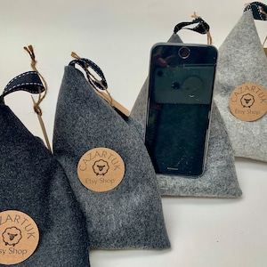 May include: Three gray felt phone stands with a black phone resting on one of them. Each stand has a brown paper tag with the text "Cazartuk Etsy Shop" and a sheep logo.