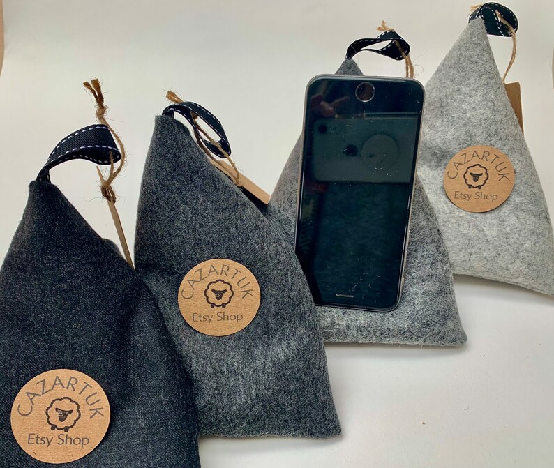 May include: Three gray felt phone stands with a black phone resting on one of them. Each stand has a brown paper tag with the text "Cazartuk Etsy Shop" and a sheep logo.