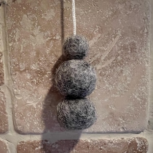 May include: Three grey felt balls strung together on a white cord. The balls are different sizes and are hanging from a ceiling.