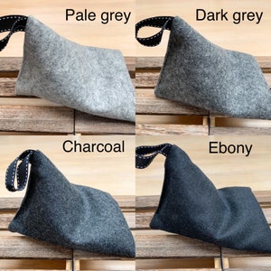 May include: Four felt pouches in different shades of gray: pale gray, dark gray, charcoal, and ebony. Each pouch has a black strap with white stitching.