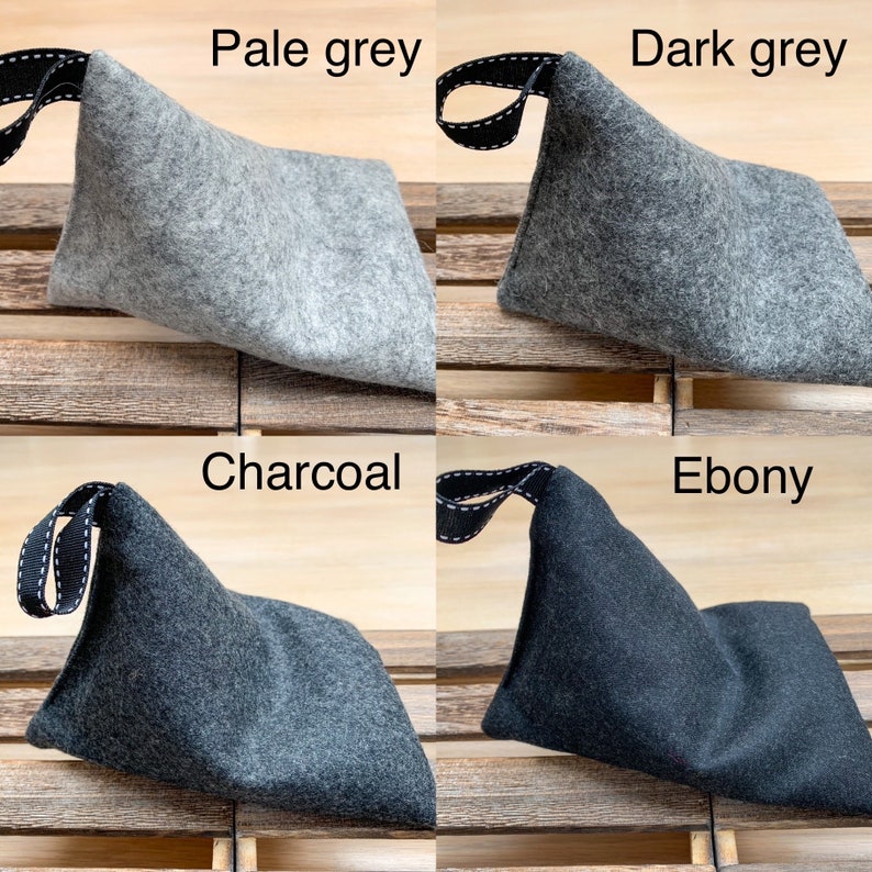 May include: Four felt pouches in different shades of gray: pale gray, dark gray, charcoal, and ebony. Each pouch has a black strap with white stitching.
