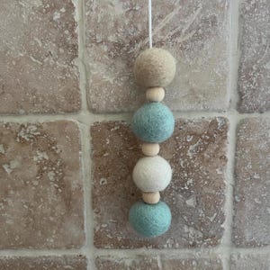 May include: A hanging mobile with four felt balls and wooden beads. The balls are in a pattern of beige, light blue, white, and light blue.