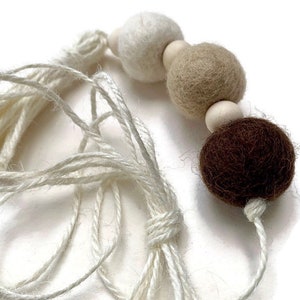 May include: A white, beige and brown felt ball garland with a white tassel. The garland is made of three felt balls and a wooden bead.