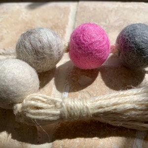May include: A garland of felt balls in shades of grey, pink, and white, with a natural fibre tassel.