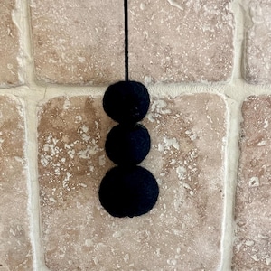 May include: Three black pom-poms hanging from a string against a beige tiled background.