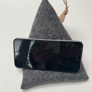 May include: A gray felt phone stand with a black loop handle. The stand is shaped like a pyramid and has a small brown tag attached to the handle.
