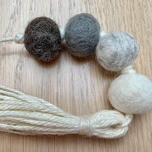 May include: A garland of felt balls in brown, grey, and white, strung together with a natural twine tassel.