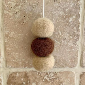 May include: Three felt balls hanging from a string. The top ball is beige, the middle ball is brown, and the bottom ball is beige.