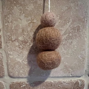 May include: A set of three felt balls in shades of pink and brown, hanging from a string. The balls are made of soft, fuzzy material and are perfect for adding a touch of whimsy to any space.