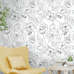 May include: A white wall with a black and white floral wallpaper pattern featuring poppy flowers. A yellow armchair with a pillow sits in front of the wall. A small wooden table with a stack of books and a potted plant sits in front of the chair.