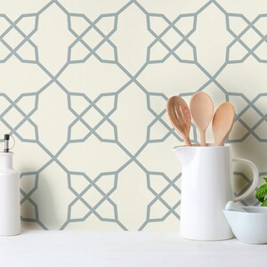 May include: A white kitchen wall with a geometric pattern wallpaper in a light blue colour. The wallpaper has a repeating pattern of intersecting lines forming a grid. There are kitchen utensils, a jug, and a mortar and pestle on a white countertop in front of the wall.