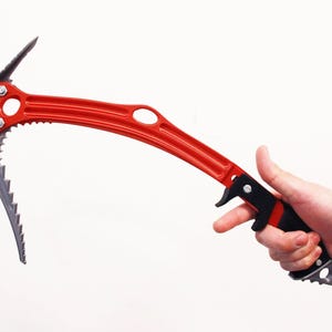 May include: A red ice axe with a curved shaft, a serrated metal pick, and an adze head. The tool features a black handle grip, a finger guard, and a pointed metal spike at the base. The construction includes multiple circular cutouts along the shaft.