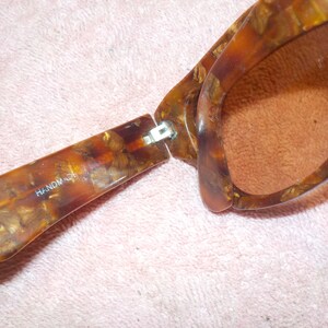 Puede incluir: Un par de gafas de sol de carey marr&oacute;n con una bisagra de metal. Las gafas est&aacute;n abiertas y las palabras "HANDMADE" son visibles en la patilla izquierda.