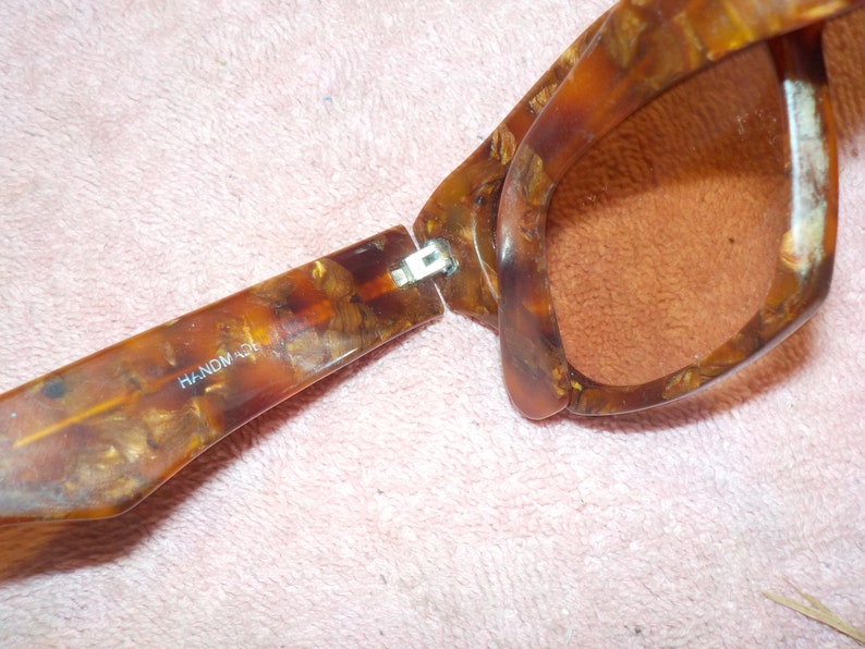 Puede incluir: Un par de gafas de sol de carey marr&oacute;n con una bisagra de metal. Las gafas est&aacute;n abiertas y las palabras "HANDMADE" son visibles en la patilla izquierda.