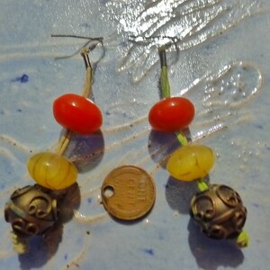 May include: A pair of earrings with red, yellow, and gold beads. The earrings are made with a wire and have a hook closure. The beads are strung on a thin cord.