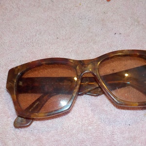 Puede incluir: Un par de gafas de sol de carey marr&oacute;n con lentes marrones. Las gafas tienen una forma rectangular y est&aacute;n hechas de pl&aacute;stico.