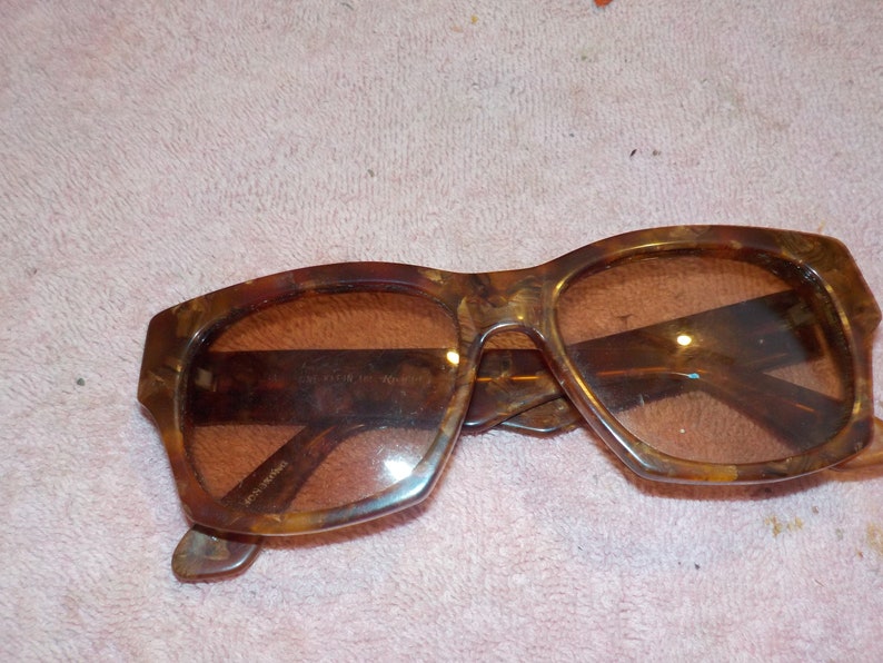 Puede incluir: Un par de gafas de sol de carey marr&oacute;n con lentes marrones. Las gafas tienen una forma rectangular y est&aacute;n hechas de pl&aacute;stico.