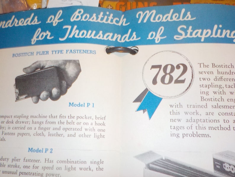 Puede incluir: Un anuncio vintage de grapadoras Bostitch, que presenta un primer plano de una peque&ntilde;a grapadora de mano y el texto "782" en una cinta azul y blanca. El anuncio destaca la variedad de modelos Bostitch disponibles para diferentes necesidades de grapado.