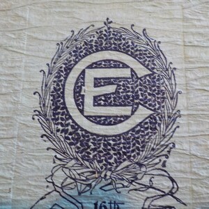 Puede incluir: Papel azul claro texturizado con un emblema azul oscuro. El emblema presenta una gran letra "E" dentro de un c&iacute;rculo con una flecha, rodeada por una corona floral. El texto "16th" es visible en la parte inferior.