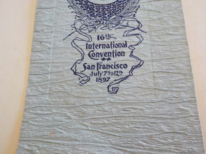 Puede incluir: Papel texturizado azul claro con texto azul oscuro. El texto dice "16&ordf; Convenci&oacute;n Internacional San Francisco 7 al 12 de julio de 1897". La parte superior del papel tiene un dise&ntilde;o floral decorativo.
