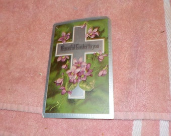 May include: A vintage Easter card with a silver cross and purple flowers on a green background. The card reads "Peaceful Easter to you".