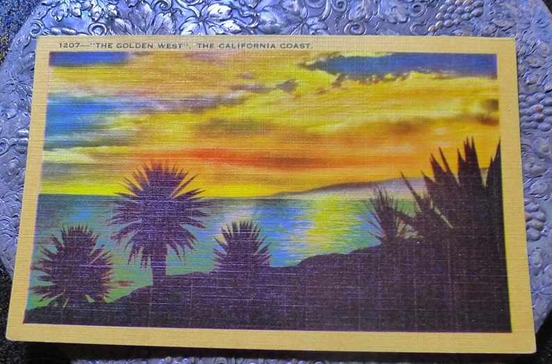 May include: A vintage postcard depicting a sunset over the ocean with palm trees silhouetted in the foreground. The text on the postcard reads "1207 - THE GOLDEN WEST - THE CALIFORNIA COAST."
