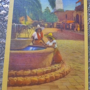 May include: A vintage postcard depicting a fountain with two women wearing sombreros in front of a building with a tall tower. The postcard reads "Olvera Street, Los Angeles, Calif."
