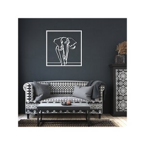 K&ouml;nnte beinhalten: Eine wei&szlig;e Linienkunst-Elefanten-Wanddekoration in einem schwarzen Rahmen, die an einer dunkelblauen Wand &uuml;ber einem schwarz-wei&szlig; gemusterten Sofa mit grauen Kissen h&auml;ngt.