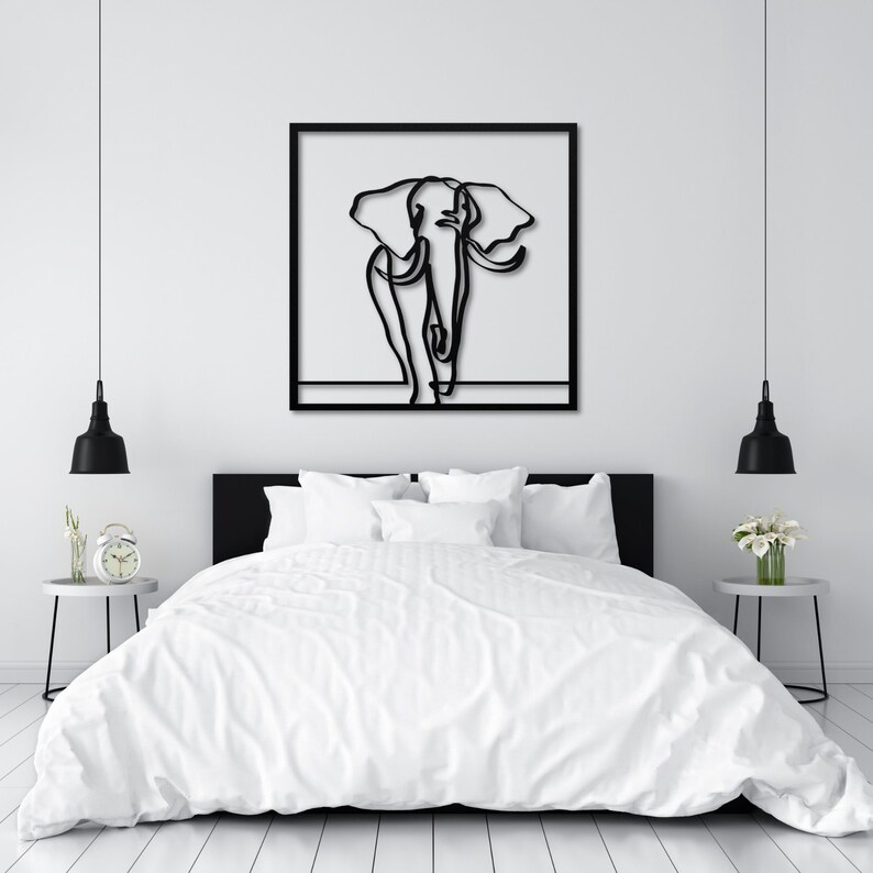 K&ouml;nnte beinhalten: Schwarz-wei&szlig;-Linienkunst-Illustration eines Elefanten in einem schwarzen Rahmen, der an einer wei&szlig;en Wand &uuml;ber einem wei&szlig;en Bett mit wei&szlig;en Bettw&auml;sche h&auml;ngt.