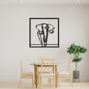 K&ouml;nnte beinhalten: Schwarz-wei&szlig;-Linienkunst eines Elefanten in einem schwarzen Rahmen. Das Kunstwerk h&auml;ngt an einer wei&szlig;en Wand &uuml;ber einem Holztisch mit St&uuml;hlen.