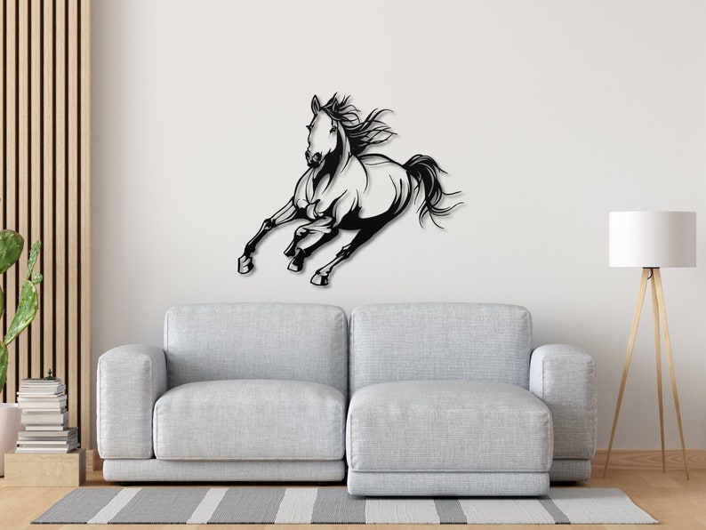 Op de afbeelding: Zwart-wit metalen wandkunst met een rennend paard. Het paard is in volle galop, met zijn manen en staart wapperend. Het kunstwerk is bevestigd aan een witte muur boven een grijze bank.