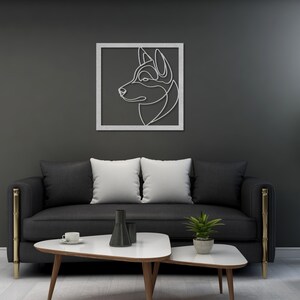 Pode incluir: Um sof&aacute; preto com duas almofadas brancas e uma moldura de metal dourado fica em frente a uma parede cinza escura. Uma impress&atilde;o de arte de linha emoldurada de uma cabe&ccedil;a de cachorro est&aacute; pendurada na parede. Uma pequena mesa de caf&eacute; branca com uma base de madeira fica em frente ao sof&aacute;. Uma pequena planta em vaso fica sobre a mesa.